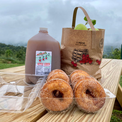 Apple cider, donuts, and a bag of apples on a wooden picnic table at Carter Mountain Orchard